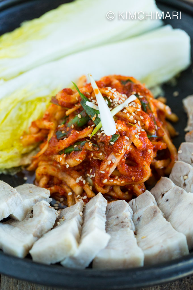 Close up of boiled pork belly, spicy radish kimchi salad and pickled cabbage leaves plated