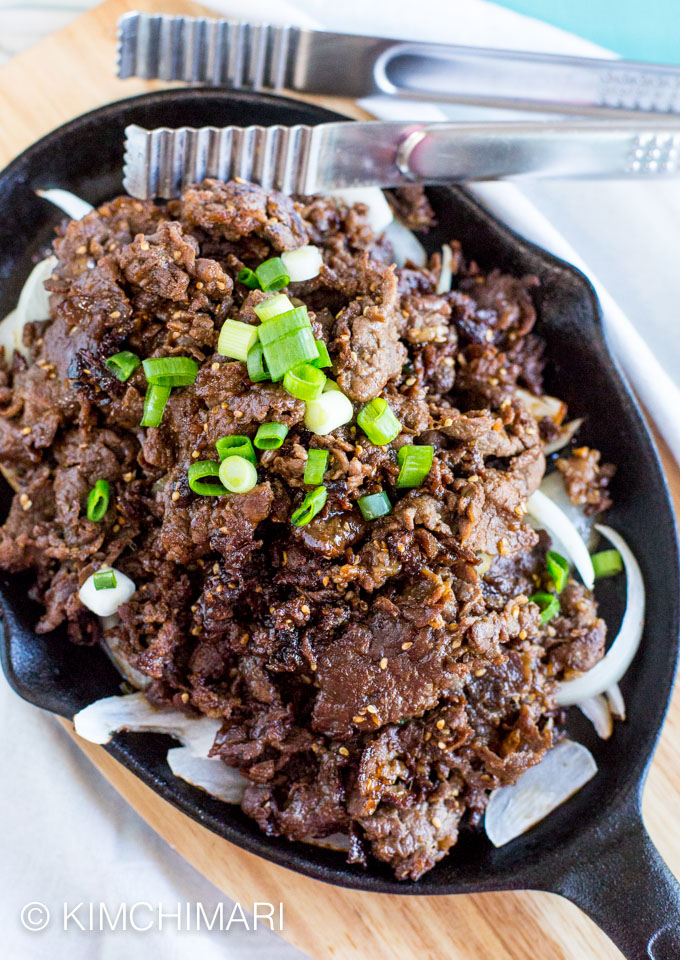 Cooked bulgogi on oval shaped cast iron skillet on wooden platter