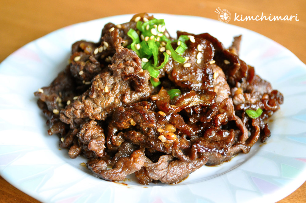 Cooked bulgogi on white blueish plate topped with chopped green onions