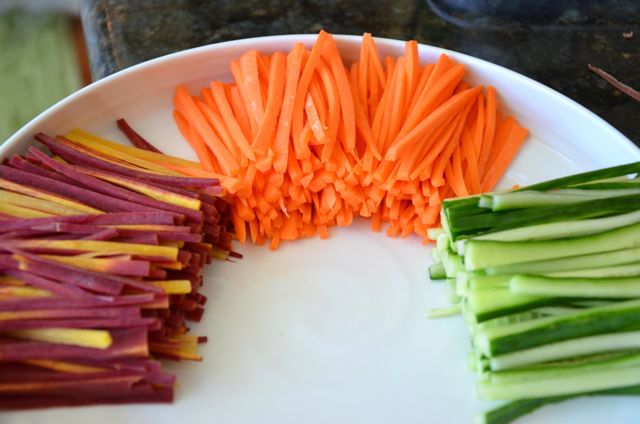 Julienned orange and purple carrots and cucumber stacked in white plate