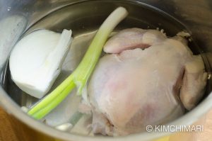 instant pot filled with water, chicken, onion, garlic and green onion