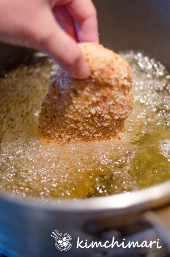 chicken katsu piece being lowered into hot oil in fryer