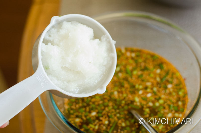 chopped onions being added to sauce in glass bowl