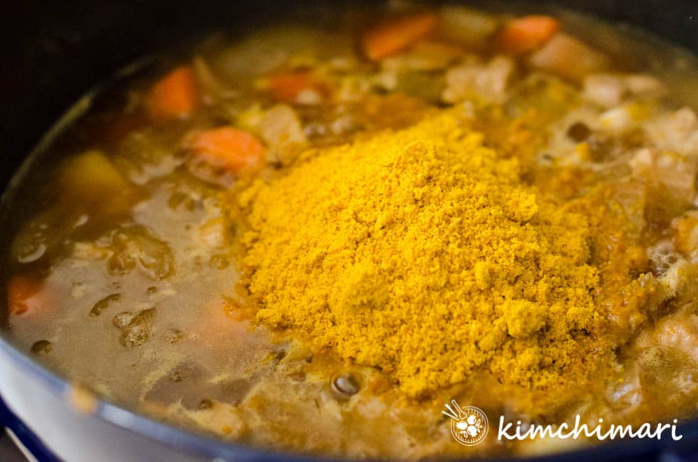 korean curry mix added to pot with cooked vegetables and meat in broth