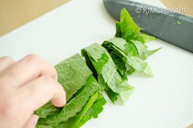 Cutting perilla leaves into thick strips with knife on cutting board