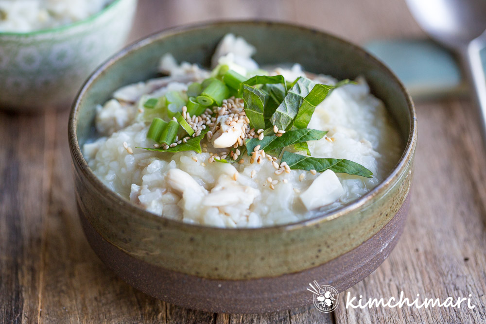 dakjuk served in greenish earthen bowl topped with perilla leaf strips, green onions and sesame seeds