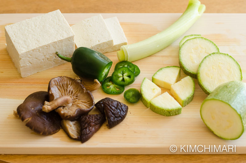 vegetable ingredients on cutting board - tofu, zucchini, green onions, shitake mushrooms and Jalapeno peppers