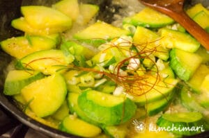 green onions and dried red pepper threads added to frying pan with squash