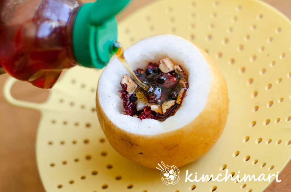 honey being poured into the hollowed out center of pear with peppercorns and jujube dates added