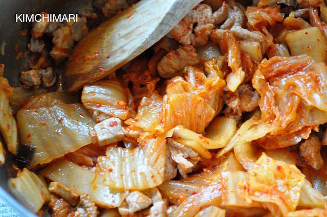 Kimchi and pork sauteeing in pot with wooden spoon