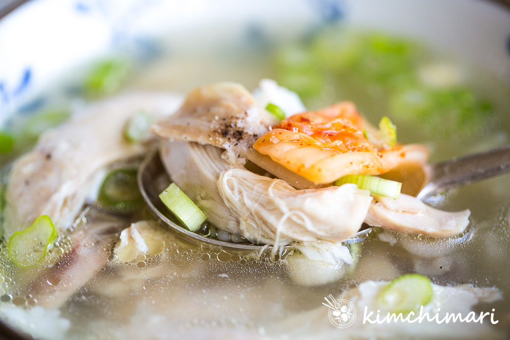 chicken, rice and kimchi piled on metal spoon on top of bowl with soup