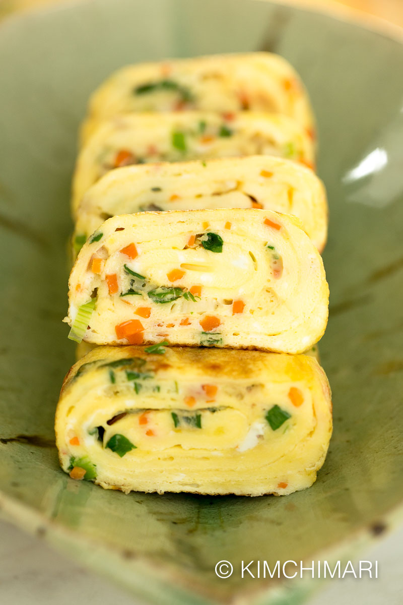 korean egg roll with carrots, ham and green onion cut into slices and plated on green dish