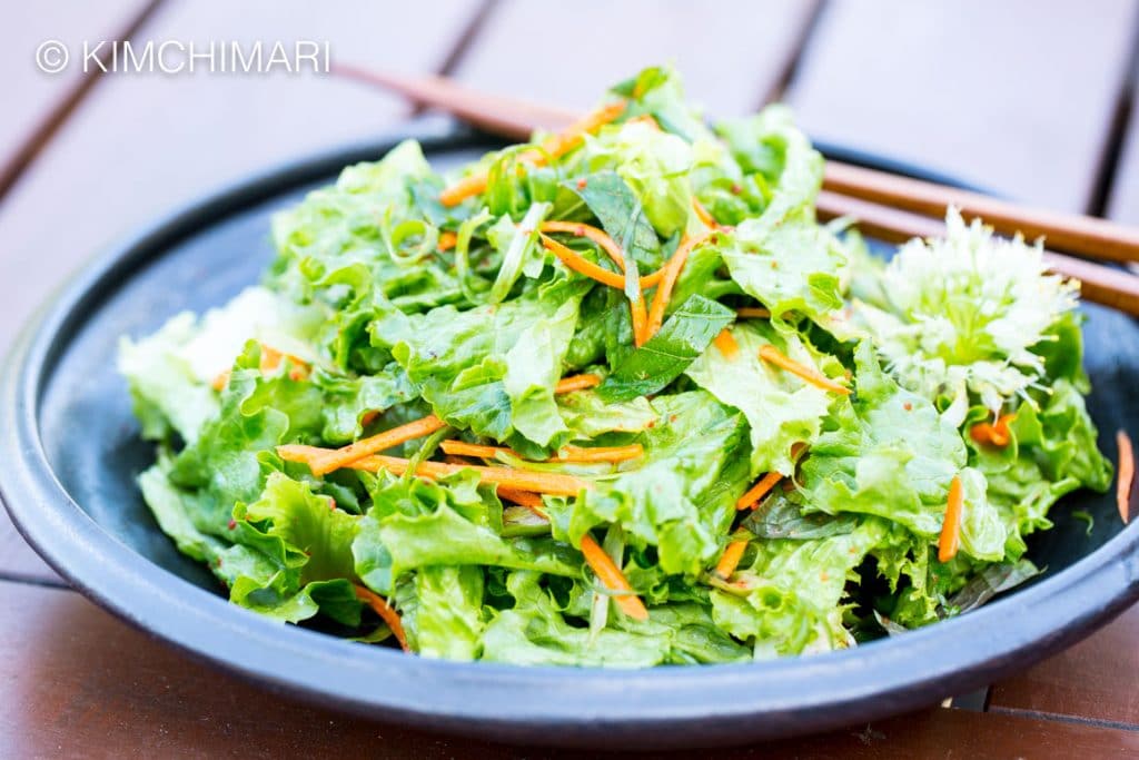 Side view of green onion salad with chopsticks in background