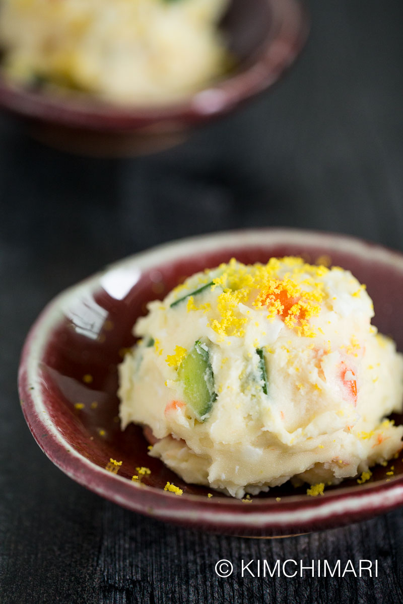 Korean potato salad served as a scoop on red bowl with grated egg yolk on top