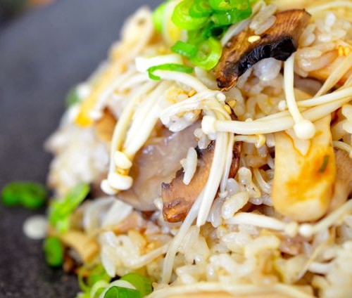 closeup of mushroom rice plated on black plate sprinkled with green onions