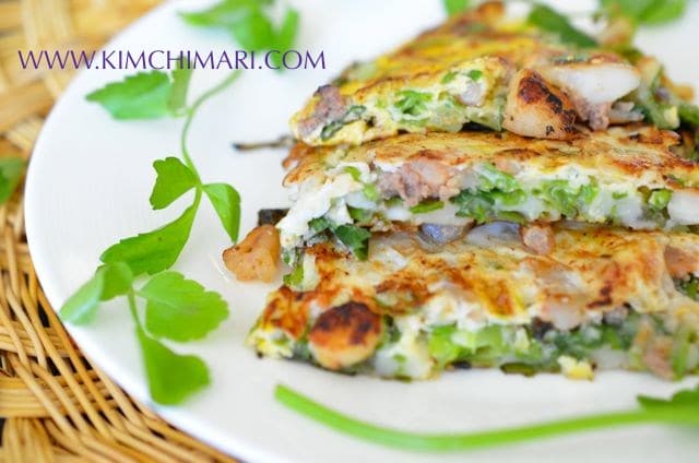 Pajeon Korean Scallion Seafood Pancake on white plate garnished with minari