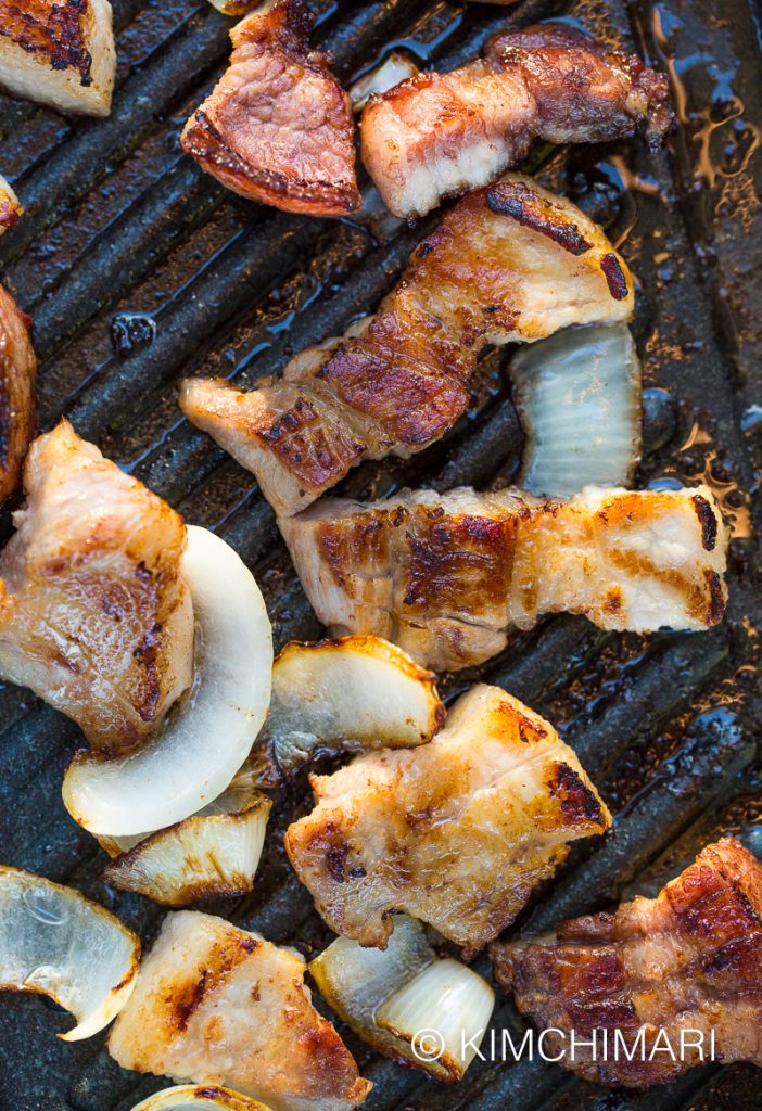 pork belly pieces and onions grilling on korean grill pan