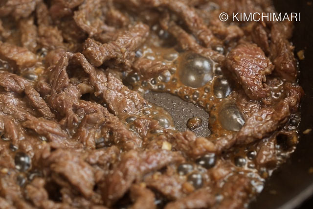 Marinated beef cooking in frying pan with sauce bubbling