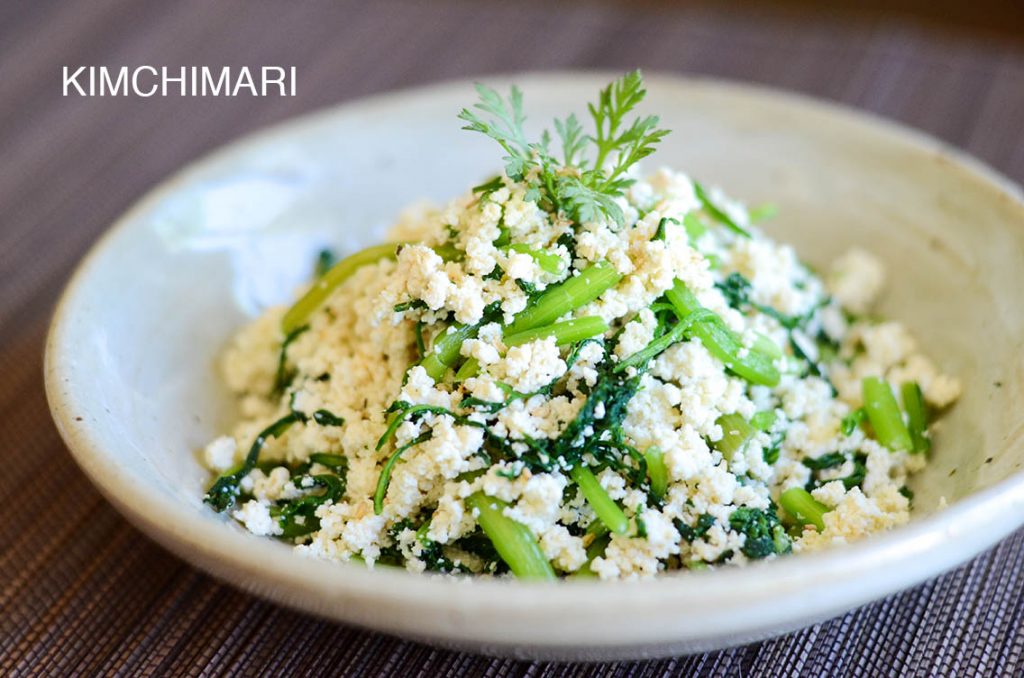 Tofu crumbles and cut crown daisies muchim in white bowl