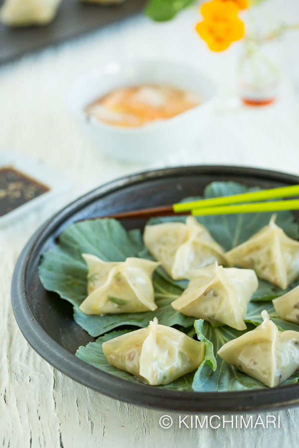 Steamed dumplings presentation with dipping sauce and nabak kimchi in the back