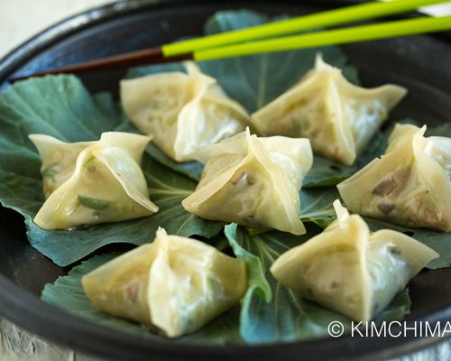 Vegetarian Dumplings or Pyeonsu served on kale leaves on black plate with green chopsticks