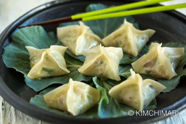 Vegetarian Dumplings or Pyeonsu served on kale leaves on black plate with green chopsticks